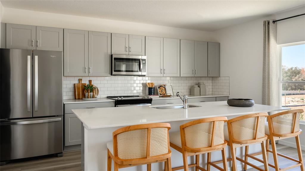 A modern kitchen features gray cabinets, white countertops, a central island, and three wooden stools — 9255 ORCHARD PARK LANE, DADE CITY, FL
