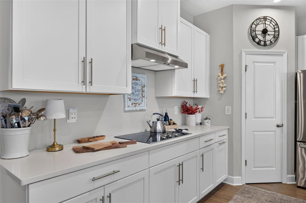 A modern kitchen features white cabinets, light countertops, a stainless steel range hood, and a clock — 14076 CRIMSON AVENUE, LAKEWOOD RANCH, FL