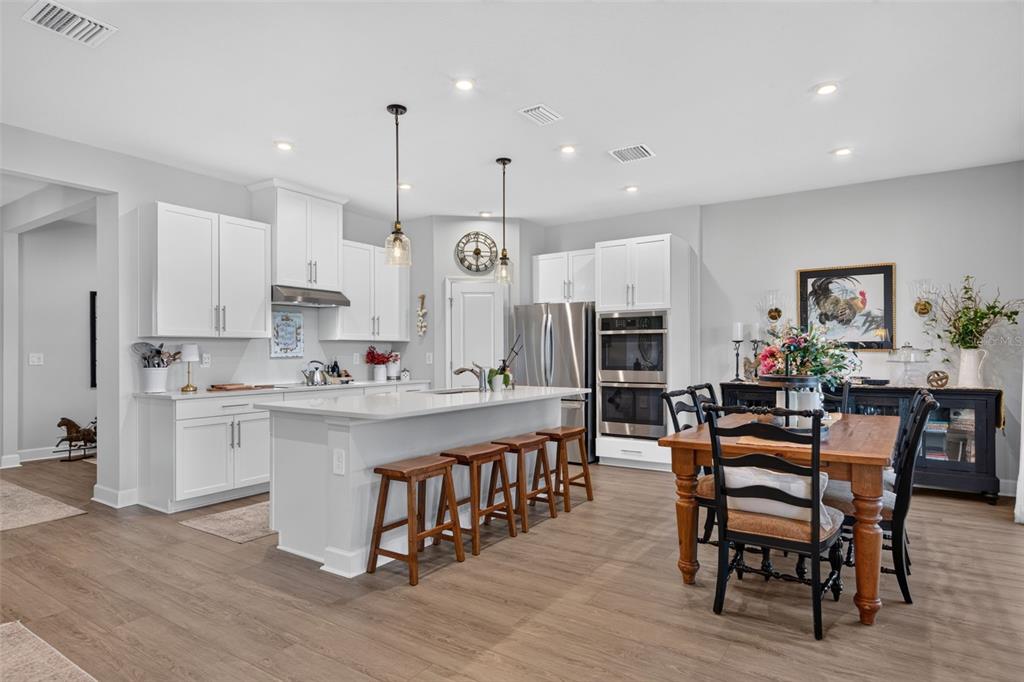 A modern kitchen features white cabinetry, a central island with bar stools, and a dining area — 14076 CRIMSON AVENUE, LAKEWOOD RANCH, FL
