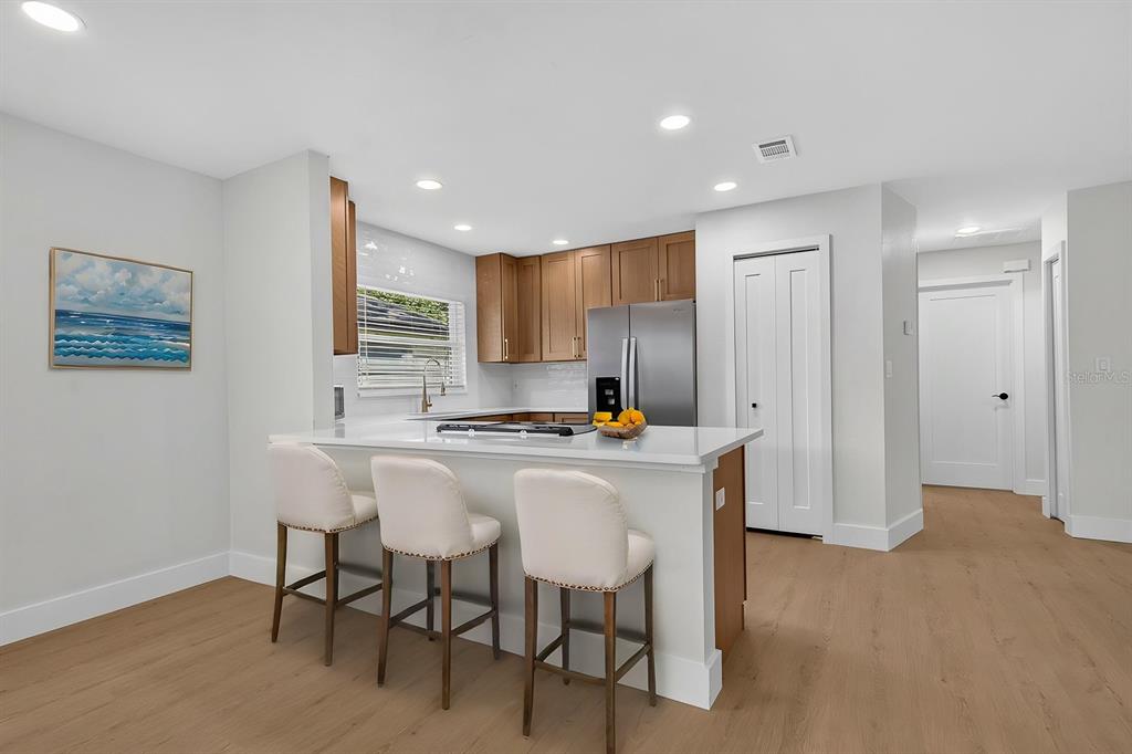 A modern kitchen features light wood cabinets, white countertops, a breakfast bar, and stainless appliances — 7037 69TH STREET N, PINELLAS PARK, FL