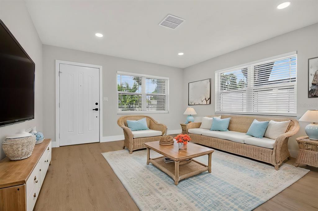 A living room features light wood flooring, wicker furniture, a white door, and large windows — 7037 69TH STREET N, PINELLAS PARK, FL