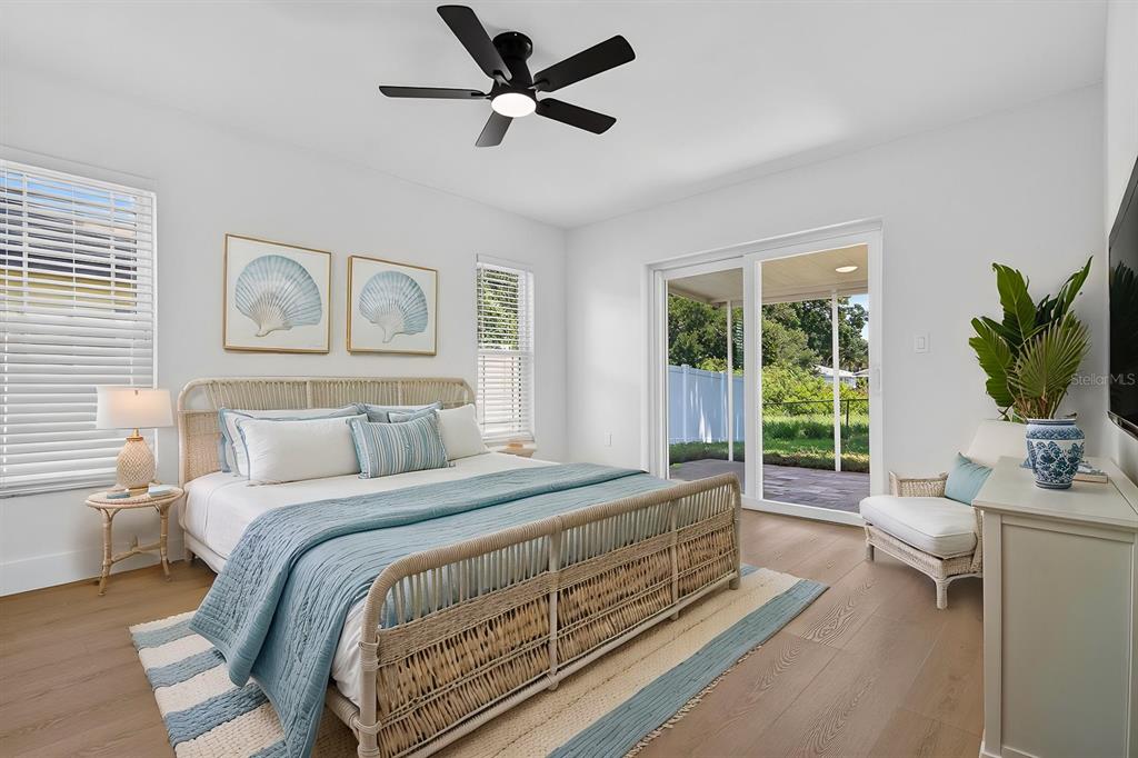 A bedroom features a rattan bed frame, light wood flooring, and sliding glass doors to a patio — 7037 69TH STREET N, PINELLAS PARK, FL
