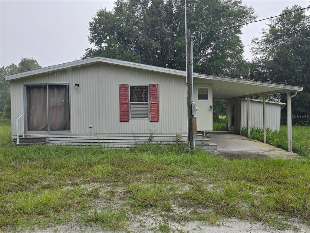 A fenced dirt lot features several small structures and trailers under a line of trees — 7810 W TWIN CANAL LANE, HOMOSASSA, FL