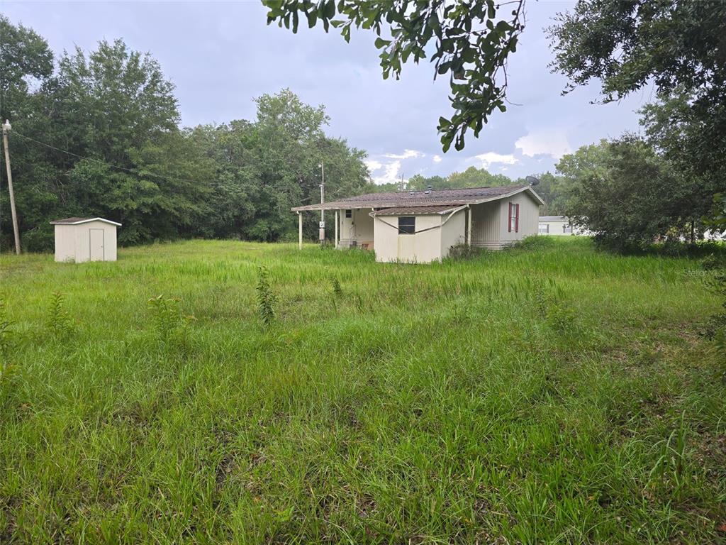 A grassy, vacant lot features mature trees and a wooden fence along the side — 7810 W TWIN CANAL LANE, HOMOSASSA, FL