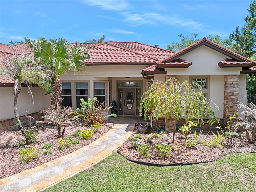A single-story house with a tiled roof, stone accents, and a stone walkway leading to the entrance — 3513 KILGALLEN COURT, ORMOND BEACH, FL