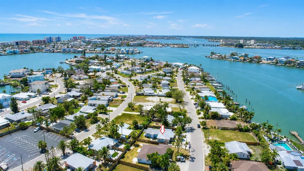 An aerial view shows a coastal neighborhood with houses, streets, and a nearby waterway — 14026 E PARSLEY DRIVE, MADEIRA BEACH, FL