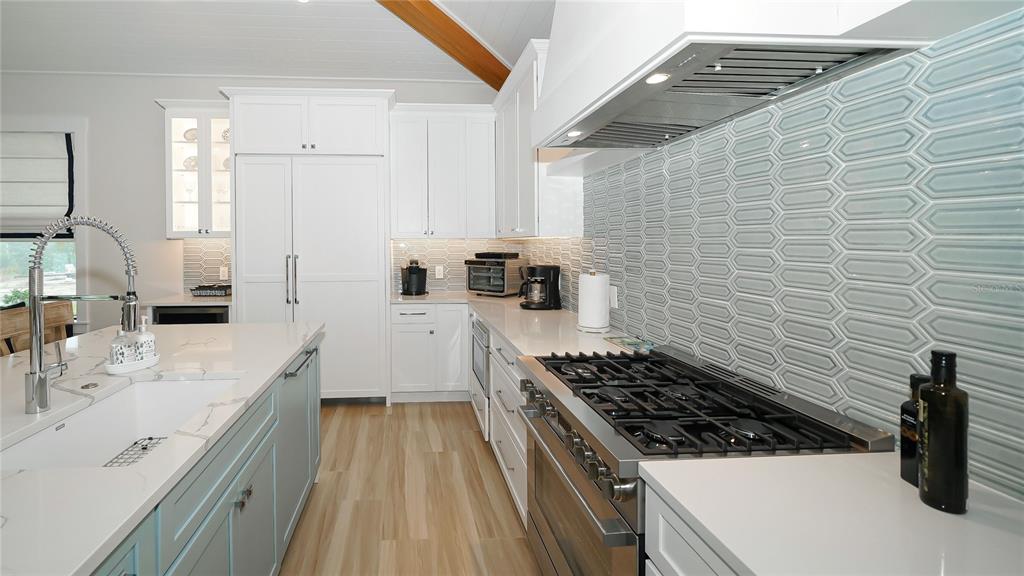 A modern kitchen features white cabinetry, a large island, stainless steel appliances, and blue tile — 307 62ND STREET, HOLMES BEACH, FL