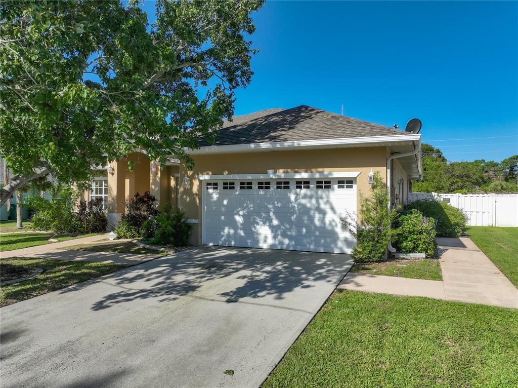 A tan single-story house with a white two-car garage and a concrete driveway — 3677 WHISPERWOOD CIRCLE, MELBOURNE, FL