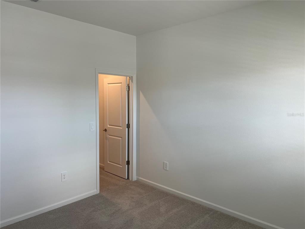 An empty room with light gray walls, beige carpet, and an open interior door — 5590 FIONA LANE, ST CLOUD, FL