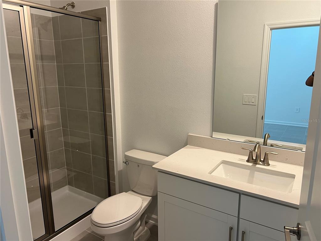 A bathroom features a glass-enclosed shower, a white vanity with a sink, and a toilet — 5590 FIONA LANE, ST CLOUD, FL