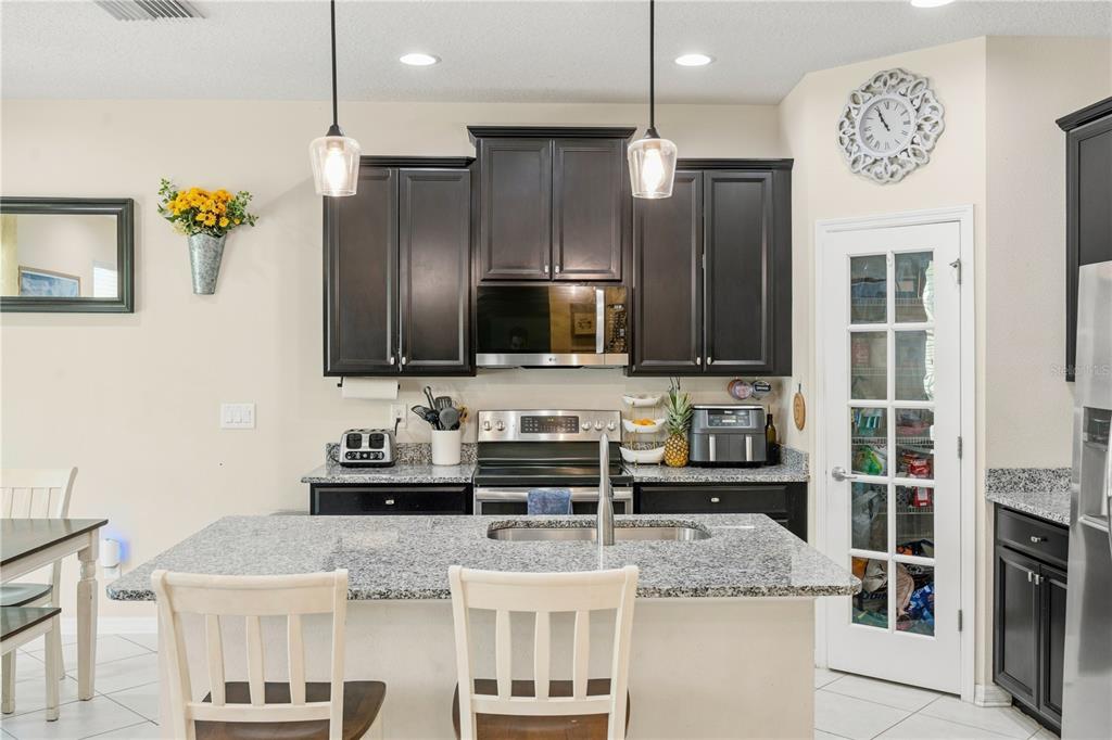 A kitchen features dark wood cabinets, granite countertops, a central island, and a pantry door — 3123 MELA COURT, HOLIDAY, FL
