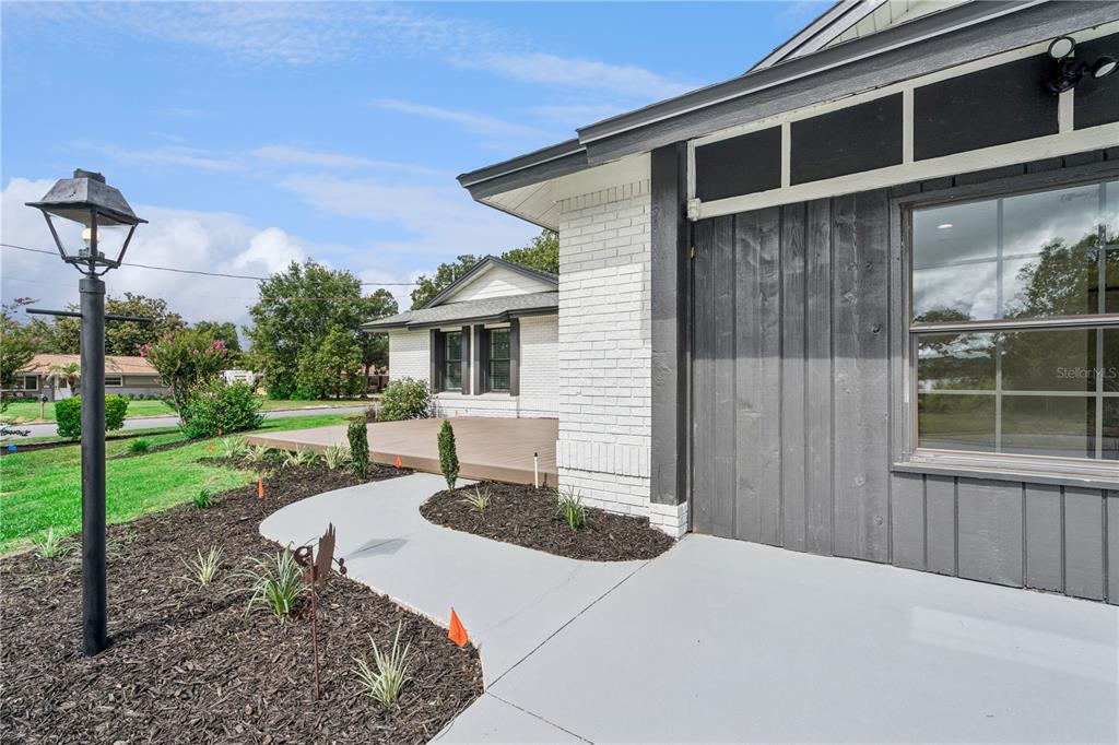 A white brick and dark wood exterior features a concrete walkway and a wooden deck — 1500 WEST AVENUE, CLERMONT, FL