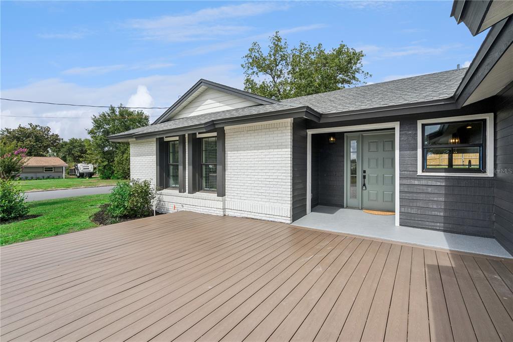 A wide wooden deck leads to the front entrance of a house with white brick — 1500 WEST AVENUE, CLERMONT, FL