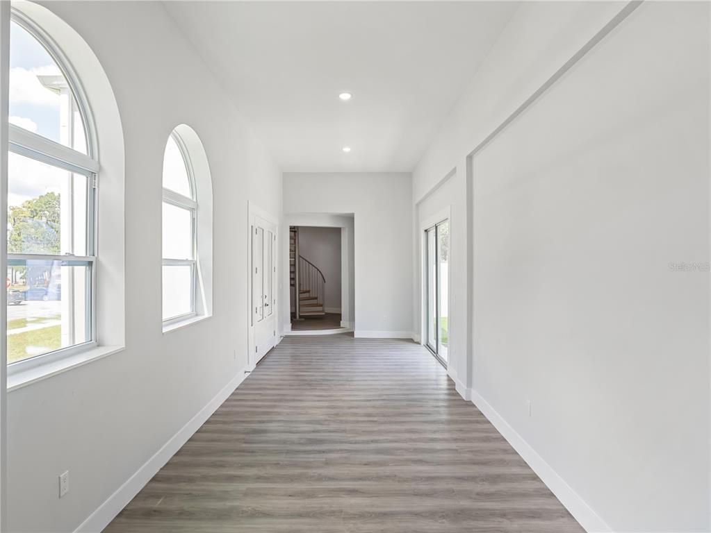 A bright hallway features light wood-look flooring, arched windows, and a view into a living room — 1190 W LAKESHORE DRIVE, CLERMONT, FL