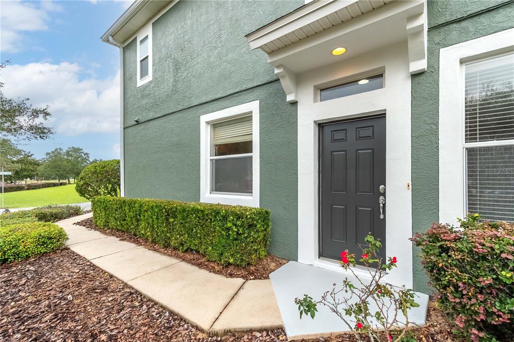 A green stucco house exterior features a dark gray front door and a concrete walkway — 4122 SW 54TH CIRCLE, OCALA, FL