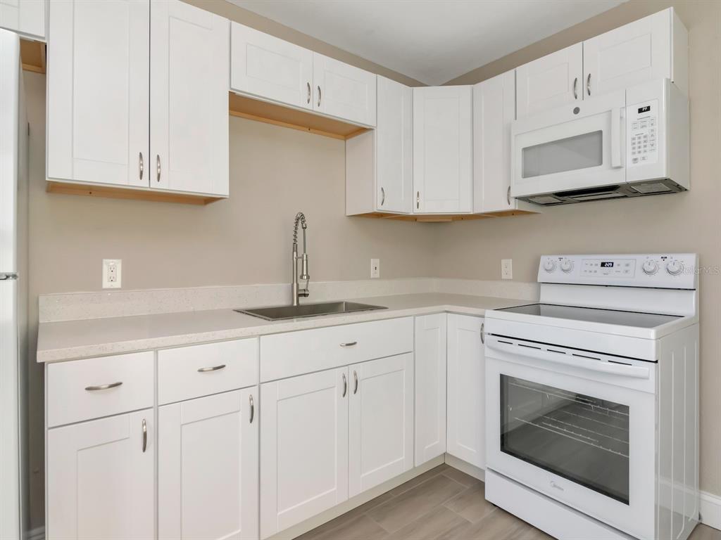 A kitchen featuring white shaker cabinets, light countertops, a stainless steel sink, and white appliances — 1207 62ND AVENUE E, BRADENTON, FL