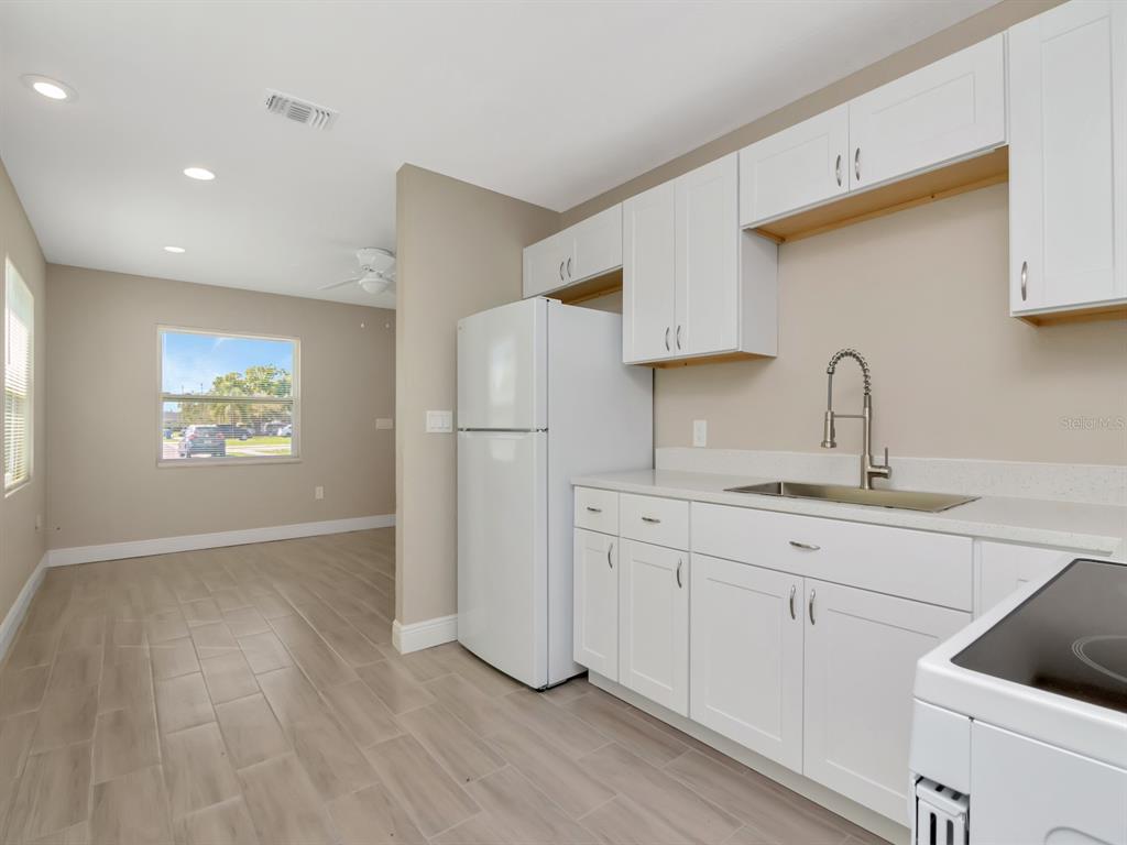 A kitchen with white cabinets, a white refrigerator, and a sink, adjacent to an open room — 1207 62ND AVENUE E, BRADENTON, FL