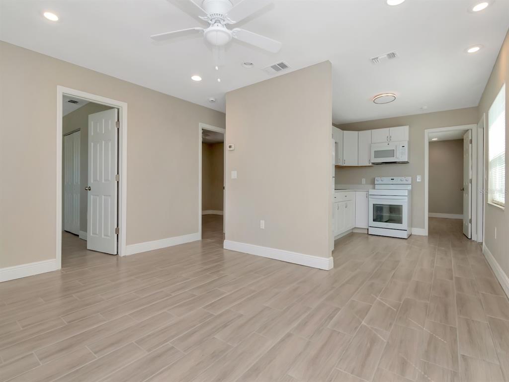 An open-concept living area with light-colored tile flooring, a ceiling fan, and a small kitchen — 1207 62ND AVENUE E, BRADENTON, FL