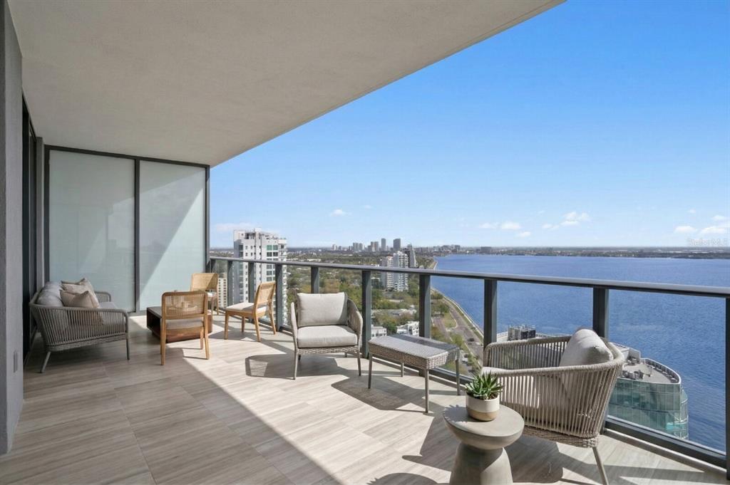 A spacious balcony with outdoor furniture overlooks a large body of water and city skyline — 3015 S YSABELLA AVENUE UNIT 2402, TAMPA, FL