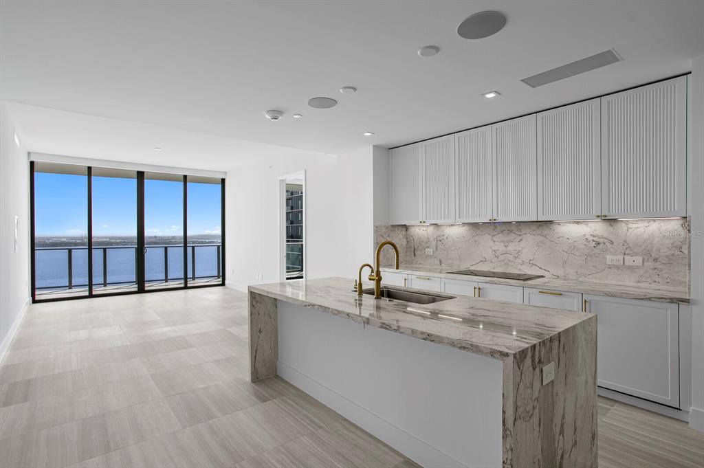 A modern kitchen features a marble island, white cabinetry, and floor-to-ceiling windows overlooking the water — 3015 S YSABELLA AVENUE UNIT 2402, TAMPA, FL
