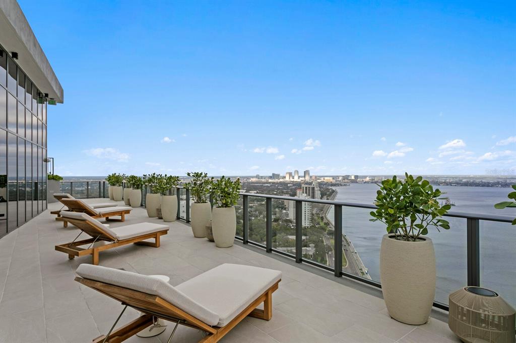 A high-rise balcony features lounge chairs, potted plants, and a panoramic view of the water — 3015 S YSABELLA AVENUE UNIT 2402, TAMPA, FL