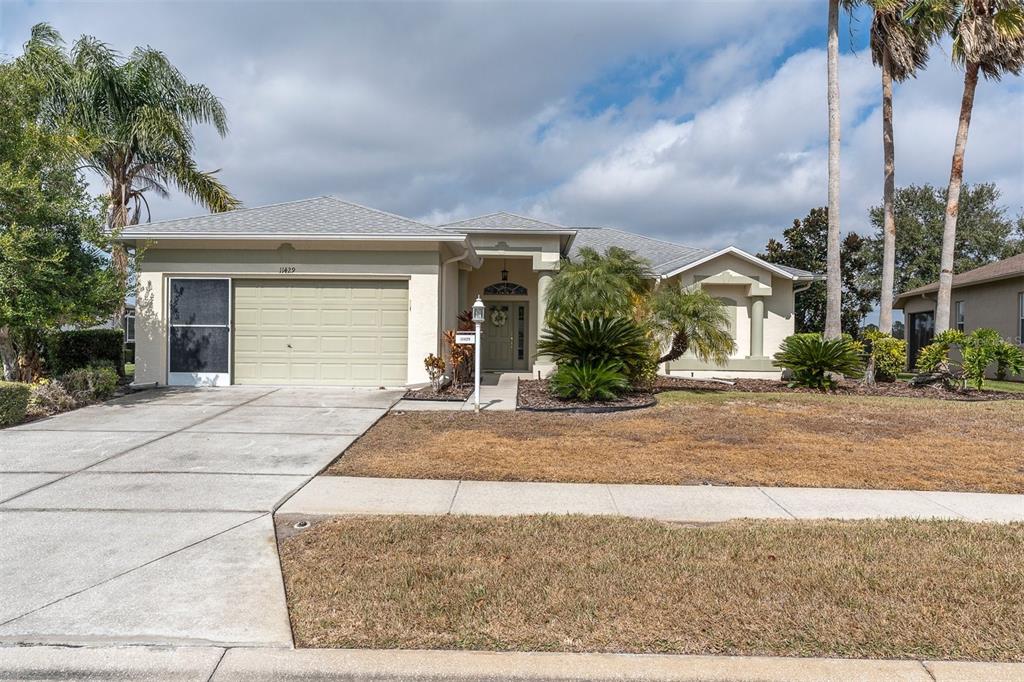 A single-story suburban house with a beige exterior, a two-car garage, and palm trees — 11429 HIDDEN COVE CT., TRINITY, FL