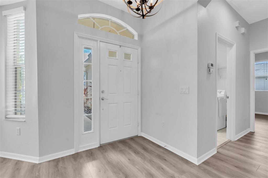 A bright entryway features light wood-look flooring, a white front door, and a transom window — 11429 HIDDEN COVE CT., TRINITY, FL
