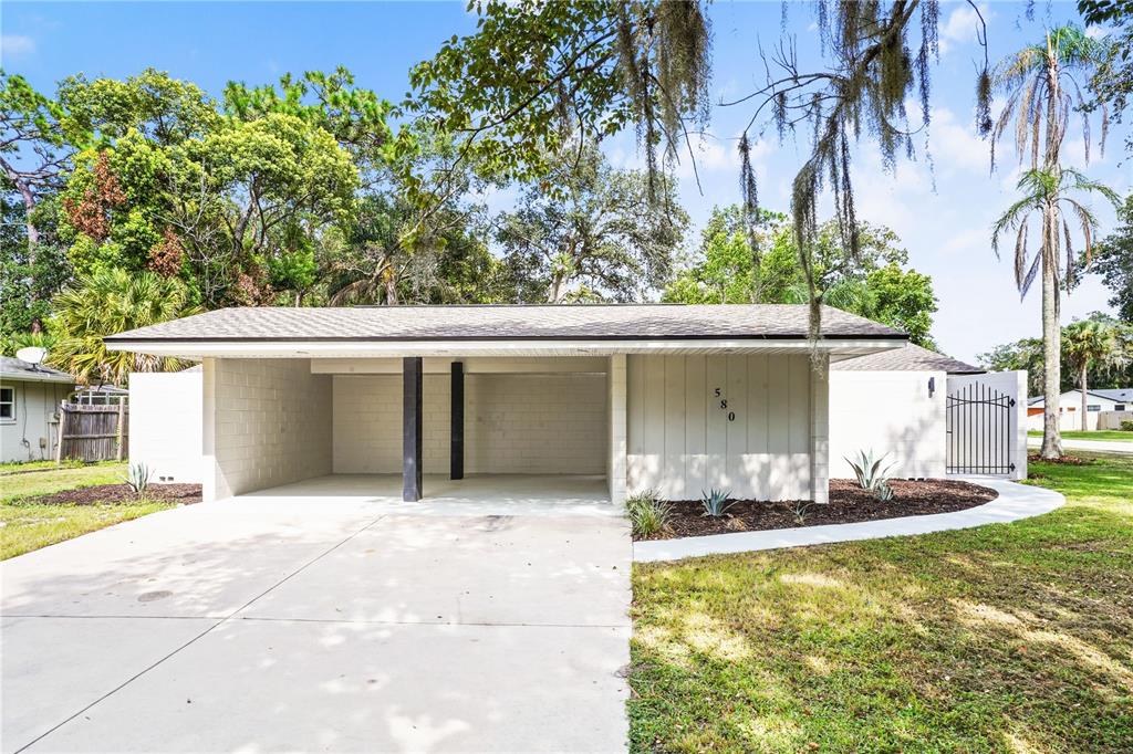A single-story house exterior features a concrete driveway, a two-car carport, and landscaping — 580 DEVONSHIRE BOULEVARD, LONGWOOD, FL