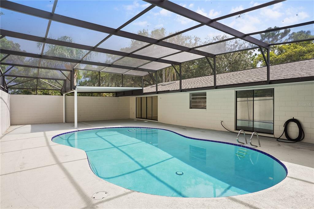 A screened-in patio features a kidney-shaped swimming pool and a white concrete block wall — 580 DEVONSHIRE BOULEVARD, LONGWOOD, FL