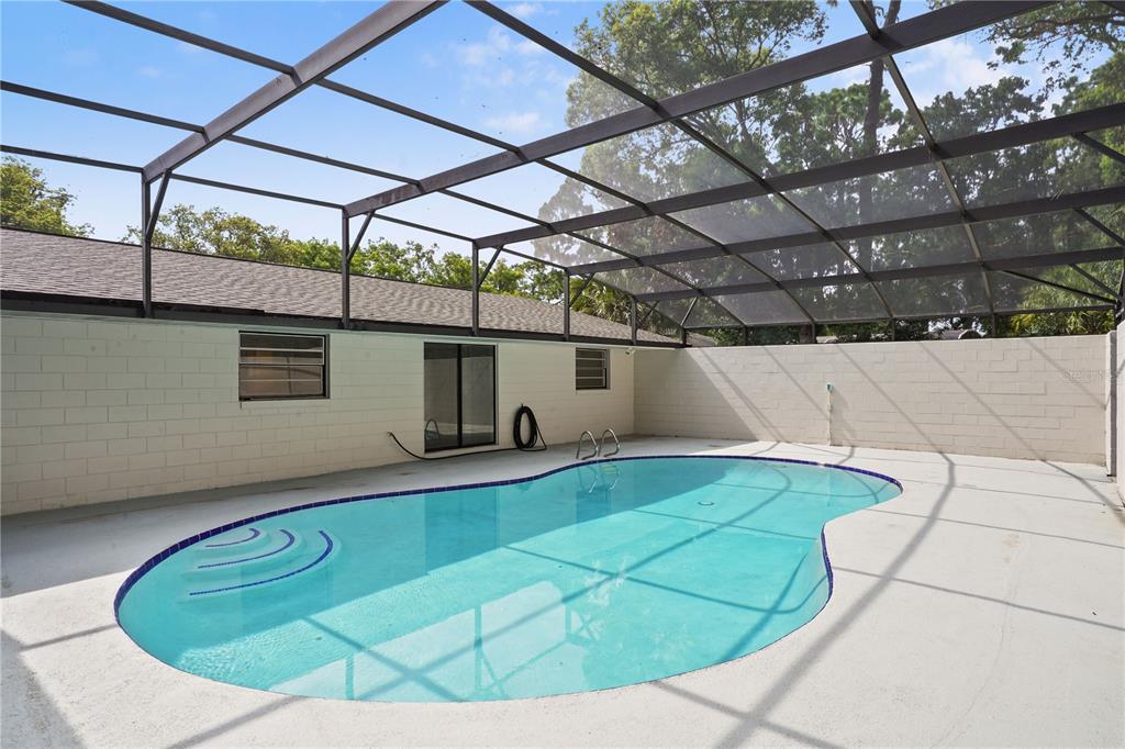 An outdoor swimming pool with a screen enclosure and a concrete deck next to a house — 580 DEVONSHIRE BOULEVARD, LONGWOOD, FL