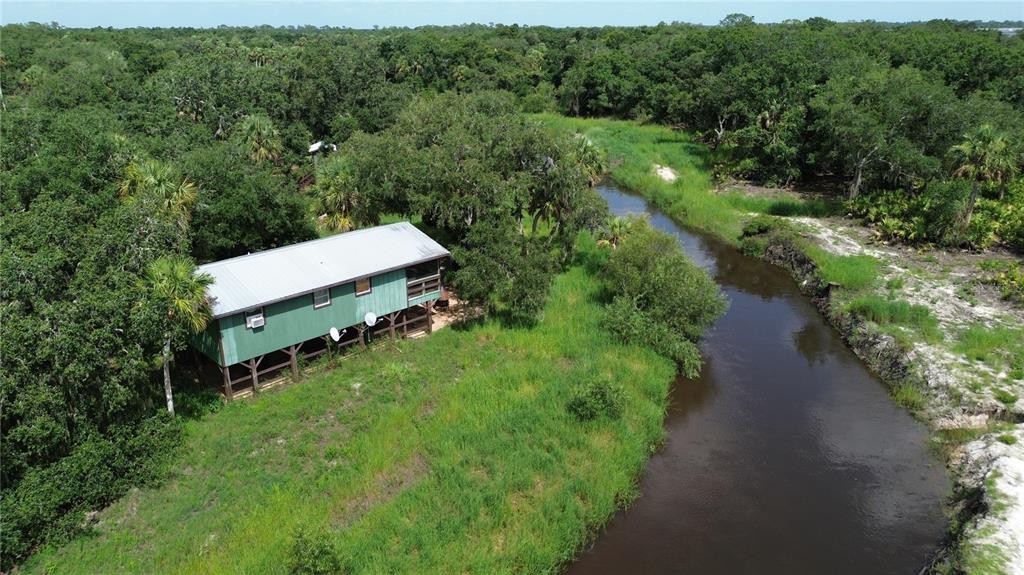 An elevated green cabin sits beside a narrow river surrounded by dense forest and vegetation — 0 SE HIGHWAY 31, ARCADIA, FL
