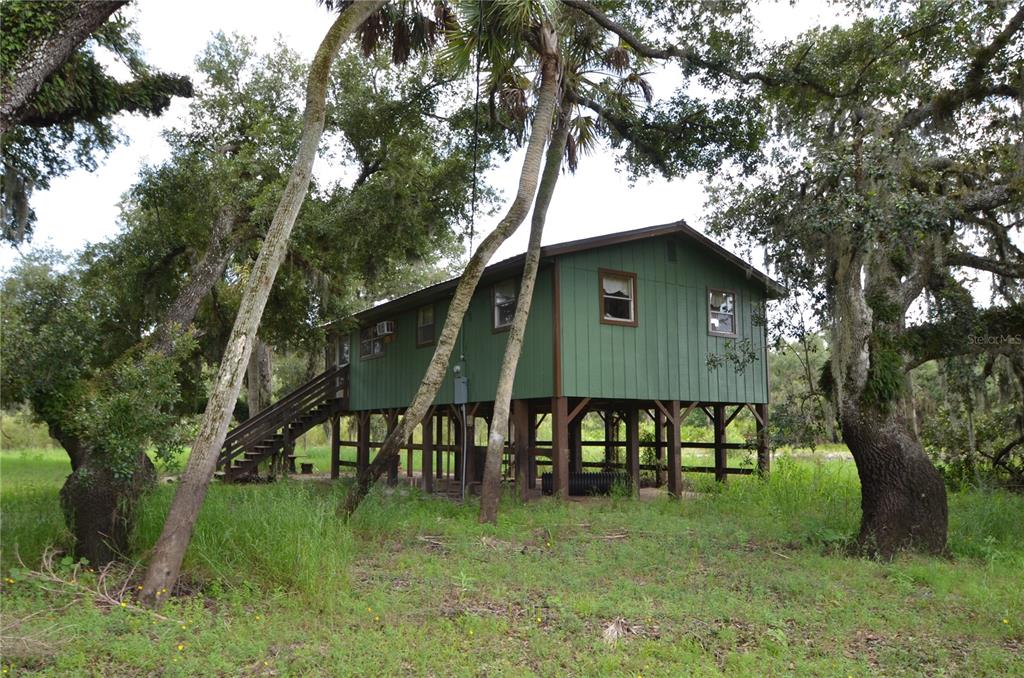 A green elevated house stands on stilts in a grassy field surrounded by large trees — 0 SE HIGHWAY 31, ARCADIA, FL