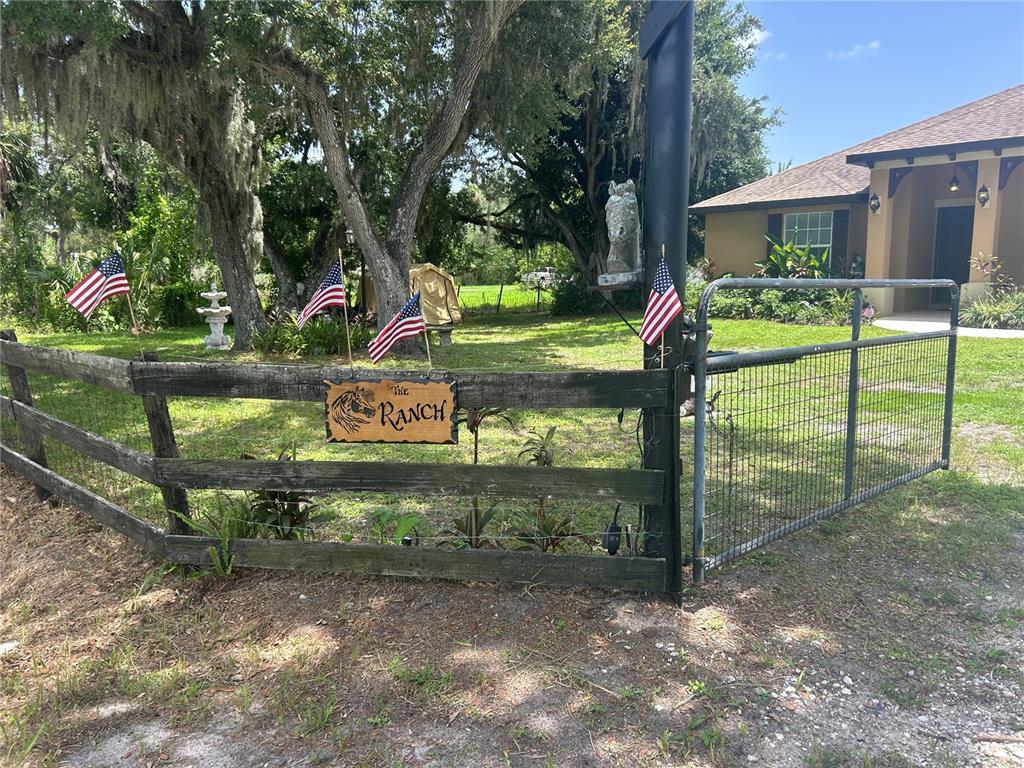 A wooden fence with American flags and a sign reading The Ranch surrounds a yard — 6416 18TH AVENUE E, BRADENTON, FL