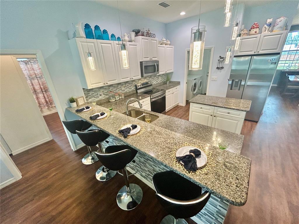 A kitchen features granite countertops, white cabinetry, stainless steel appliances, and a breakfast bar — 6416 18TH AVENUE E, BRADENTON, FL