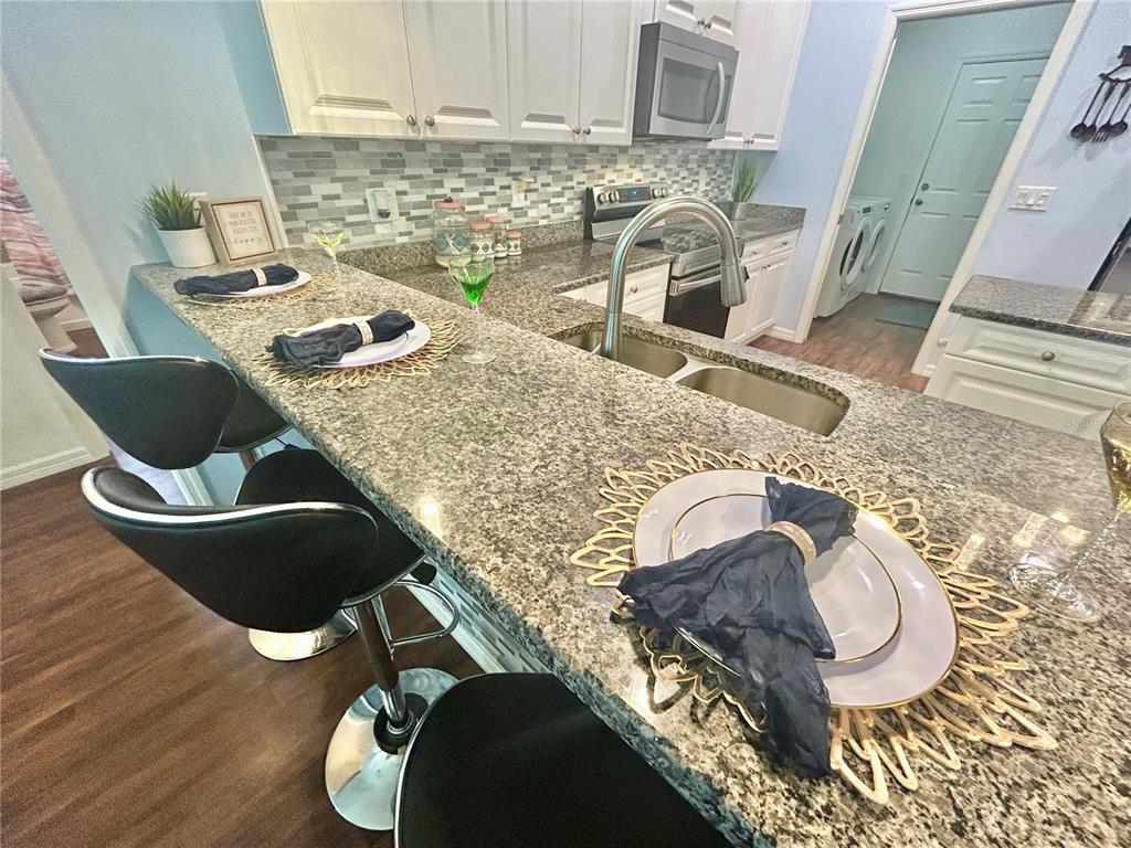 A kitchen features granite countertops, white cabinetry, a breakfast bar with stools, and stainless appliances — 6416 18TH AVENUE E, BRADENTON, FL