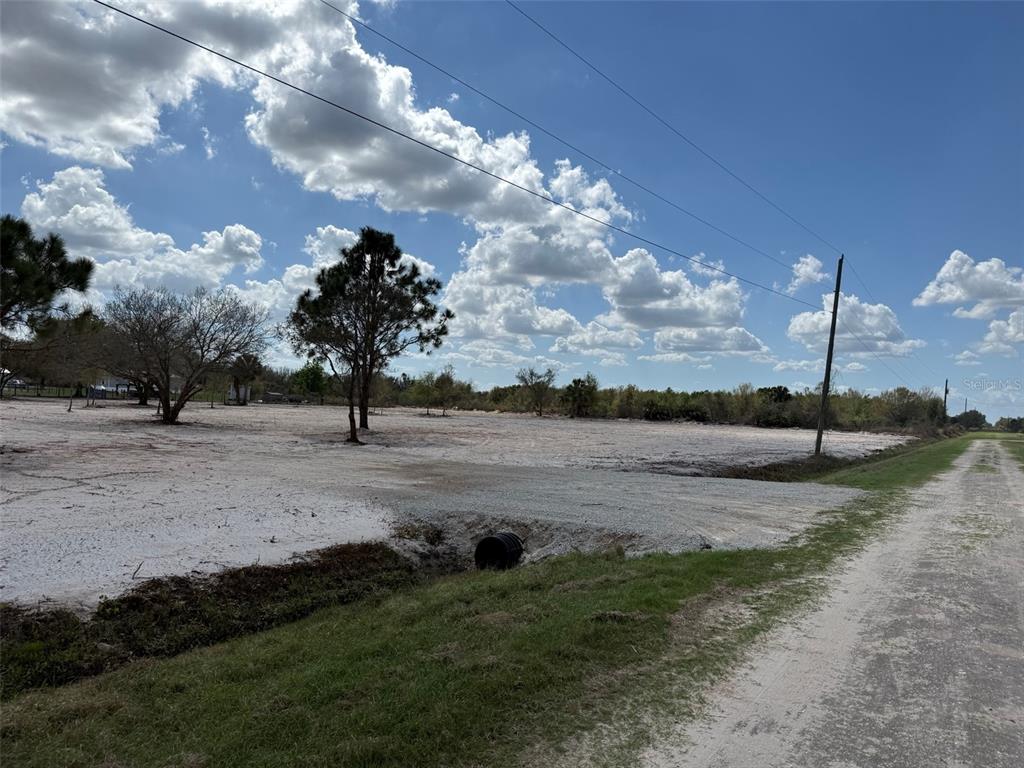A cleared, sandy vacant lot features a culvert pipe and scattered trees under a blue sky — 14416 NW 252ND STREET, OKEECHOBEE, FL