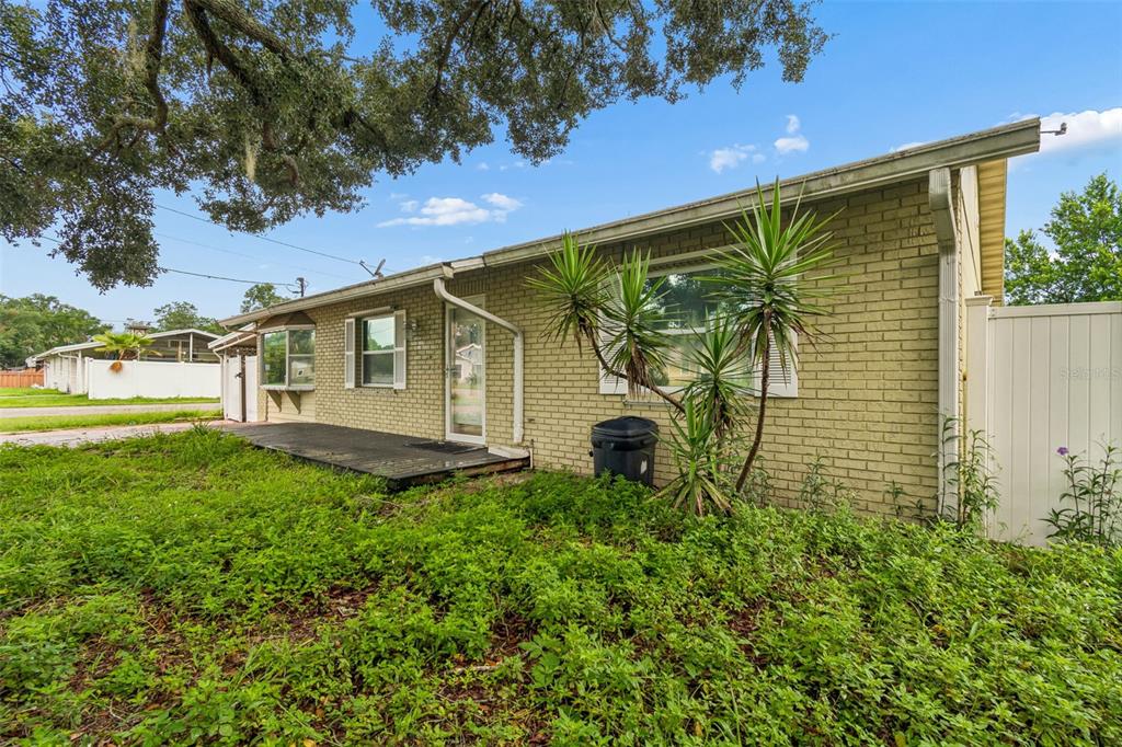 A single-story brick house with a wooden deck and overgrown lawn under a large tree — 38621 NORTH AVENUE, ZEPHYRHILLS, FL