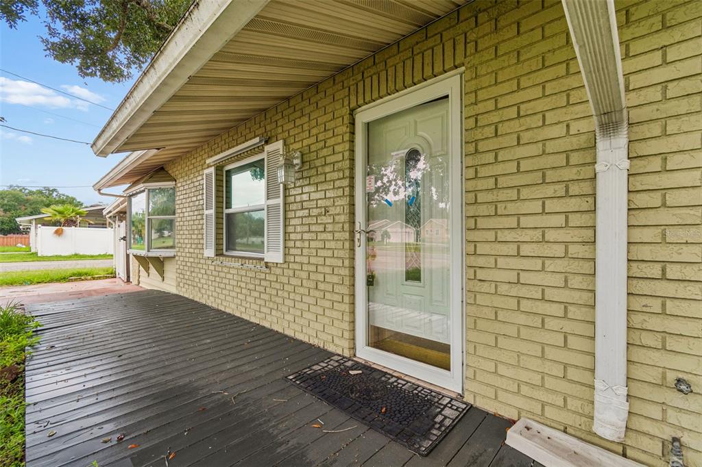 A light green brick house exterior features a dark wooden porch and a glass storm door — 38621 NORTH AVENUE, ZEPHYRHILLS, FL