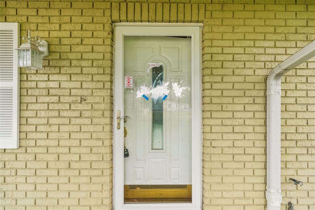 A white front door with a glass insert is set into a light yellow brick wall — 38621 NORTH AVENUE, ZEPHYRHILLS, FL
