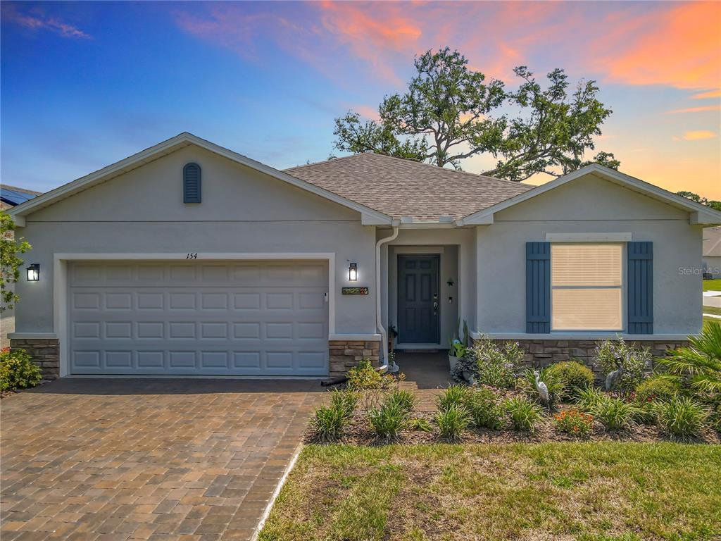 A single-story house with a gray garage, stone accents, and a paved driveway at sunset — 154 JONES FISH CAMP ROAD, EDGEWATER, FL