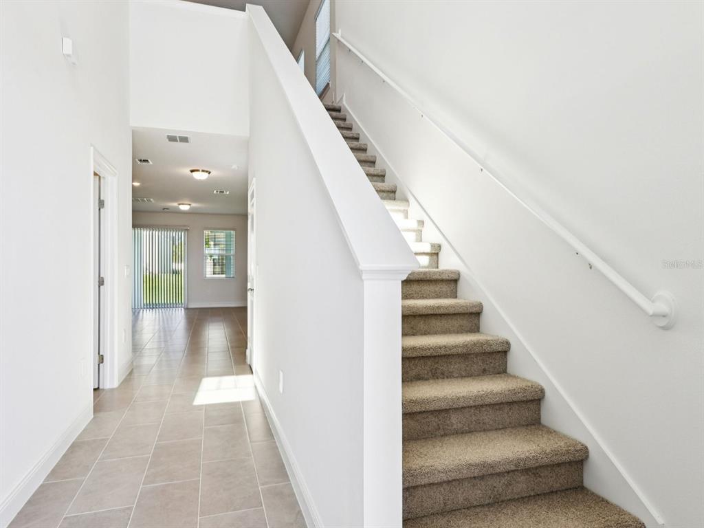 A hallway with tile flooring leads to a living area past a carpeted staircase — 2194 WILDBERRY WAY, MINNEOLA, FL