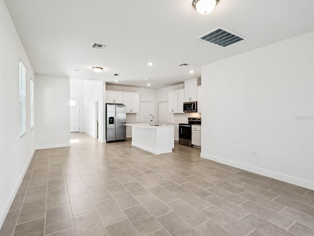 An open-concept kitchen and living area with white cabinets, stainless steel appliances, and tile flooring — 2194 WILDBERRY WAY, MINNEOLA, FL