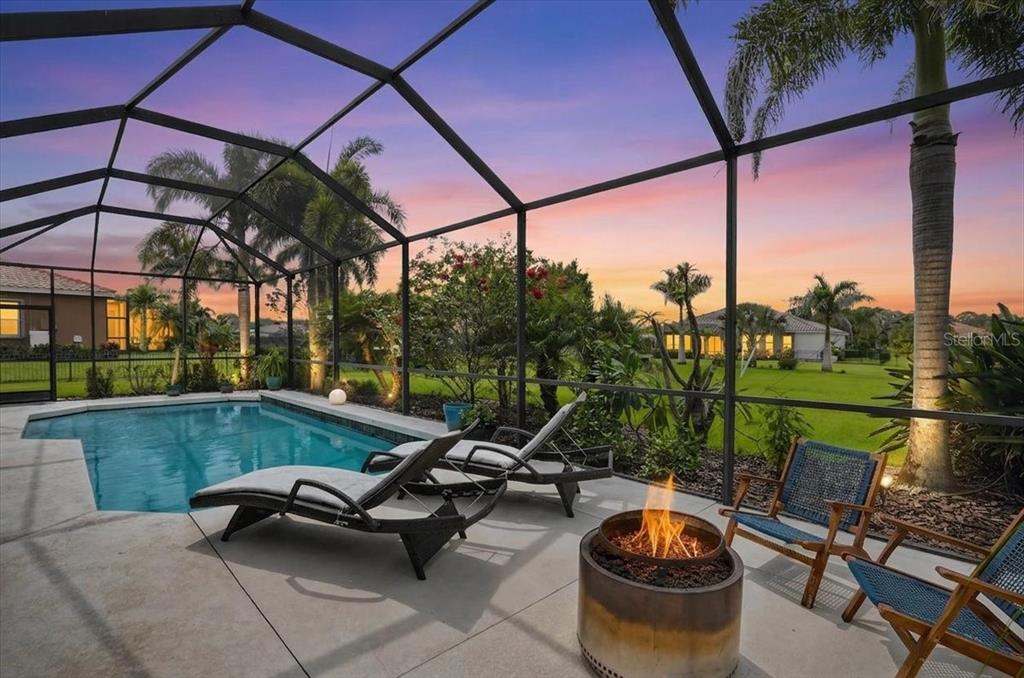 A screened-in pool patio features lounge chairs, a fire pit, and a sunset view — 17009 1ST DRIVE E, BRADENTON, FL