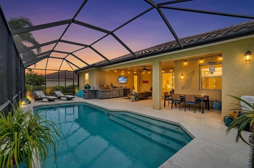 A screened-in patio features a swimming pool, outdoor kitchen, and dining area at sunset — 17009 1ST DRIVE E, BRADENTON, FL