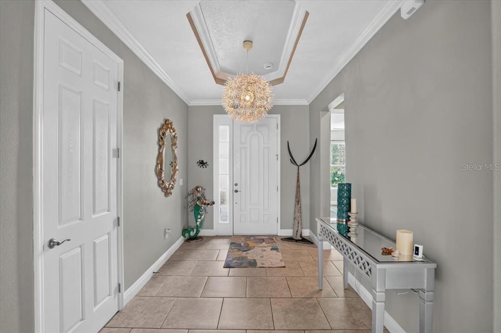 A tiled entryway features a tray ceiling, a decorative chandelier, and a mirrored console table — 17009 1ST DRIVE E, BRADENTON, FL