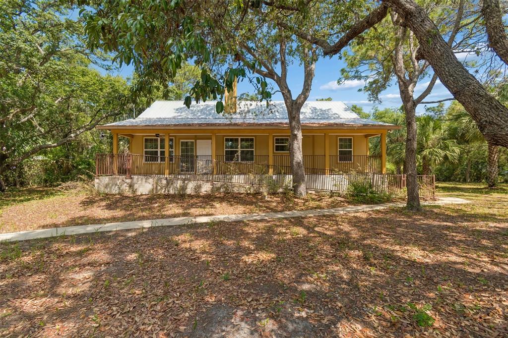 A one-story house with a metal roof and a wraparound porch sits among mature trees — 11274 S RIVIERA DRIVE, HOMOSASSA, FL