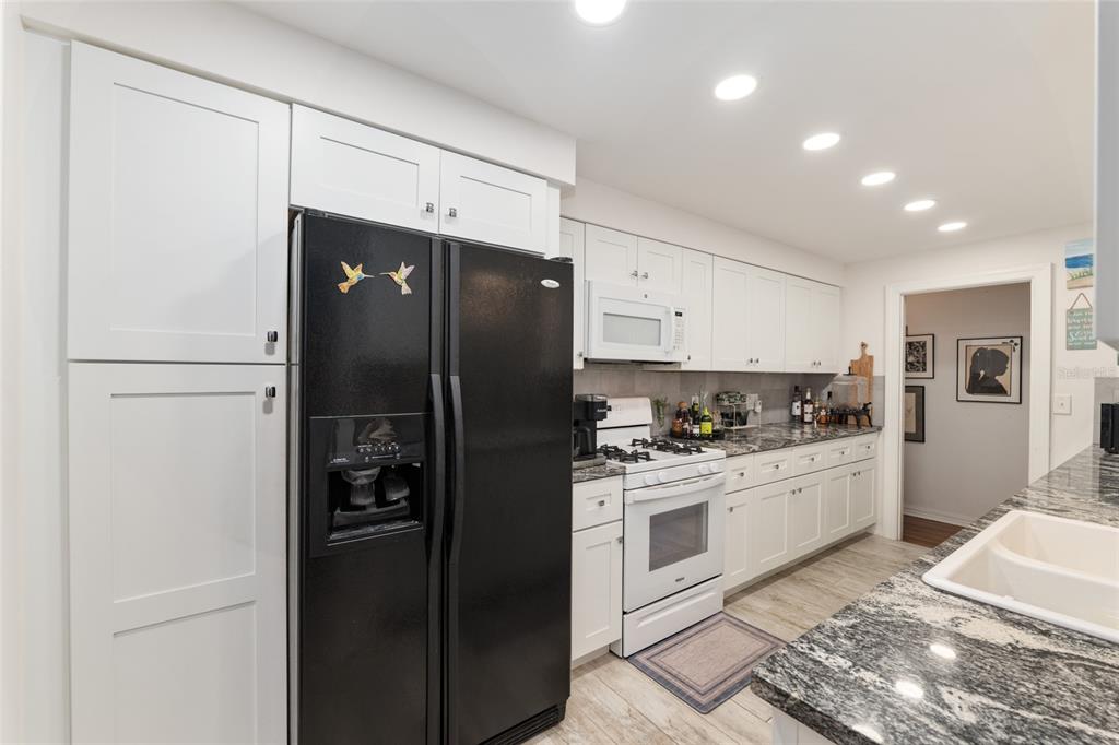 A galley kitchen features white cabinets, dark granite countertops, and light wood-look tile flooring — 1210 SE 14TH AVENUE, OCALA, FL