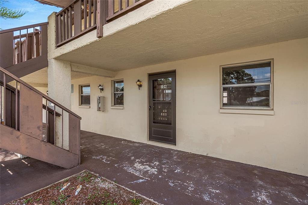 A two-story apartment building exterior features a wooden balcony, stairs, and a white picket fence — 5521 BAY BOULEVARD UNIT 104, PORT RICHEY, FL