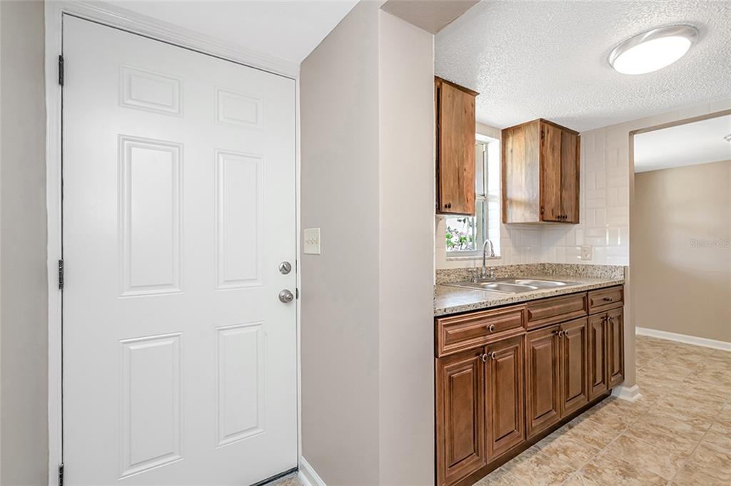 An exterior view of a ground-level apartment entrance with a brown door and stairs — 5521 BAY BOULEVARD UNIT 104, PORT RICHEY, FL