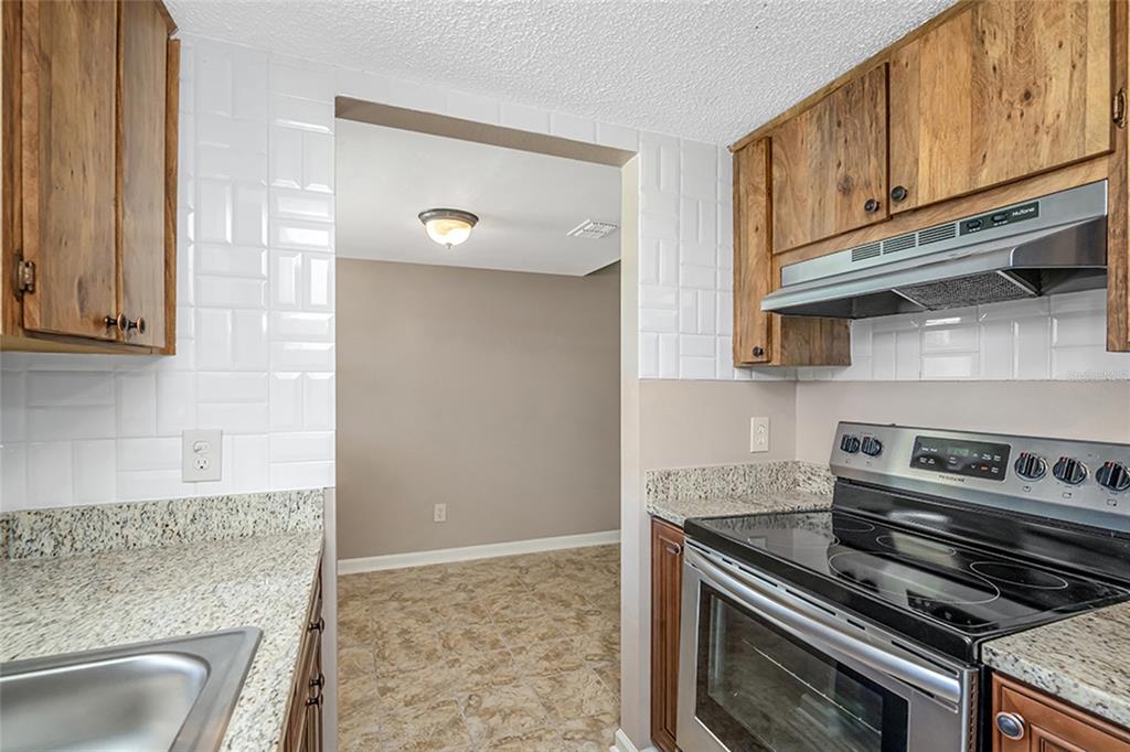 A kitchen features wood cabinets, stainless steel appliances, and granite countertops — 5521 BAY BOULEVARD UNIT 104, PORT RICHEY, FL